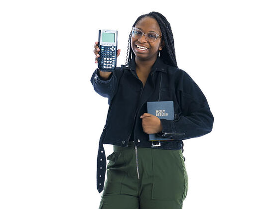 A student holding a Bible and a calculator stands in front of a white background.