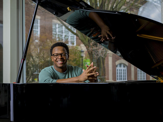 A student smiles while sitting at a piano.