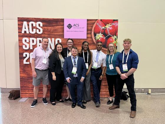 McDaniel students and faculty pose for a group photo in front of an ACS conference sign