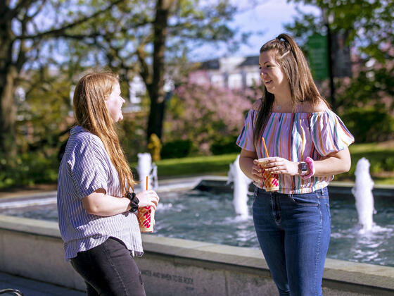 Two students in conversation near fountain on campus.