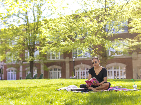 Student reading book sitting on lawn on campus.