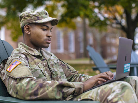ROTC student in uniform sitting in outdoor chair on campus.