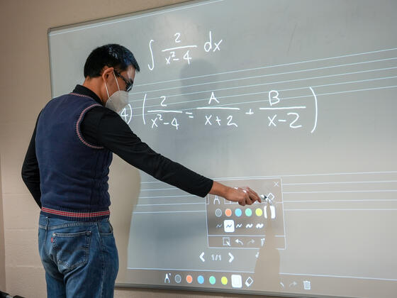 A student writes equations on a whiteboard.