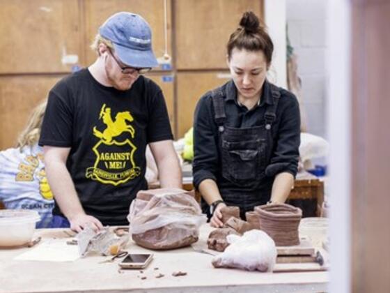 A male and female student work at a table with a block of clay on it.