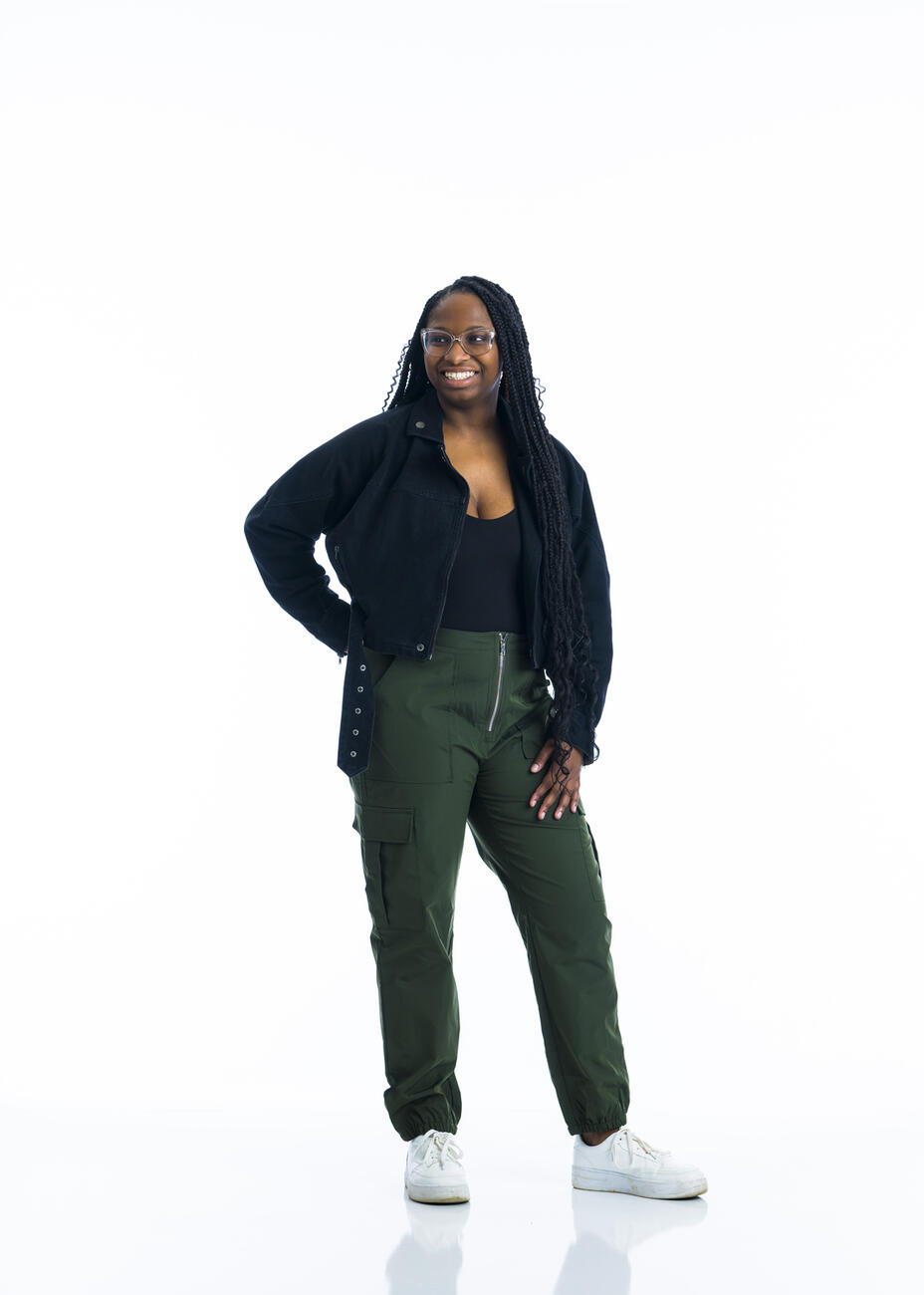 A student stands with one hand on her hip in front of a white background.