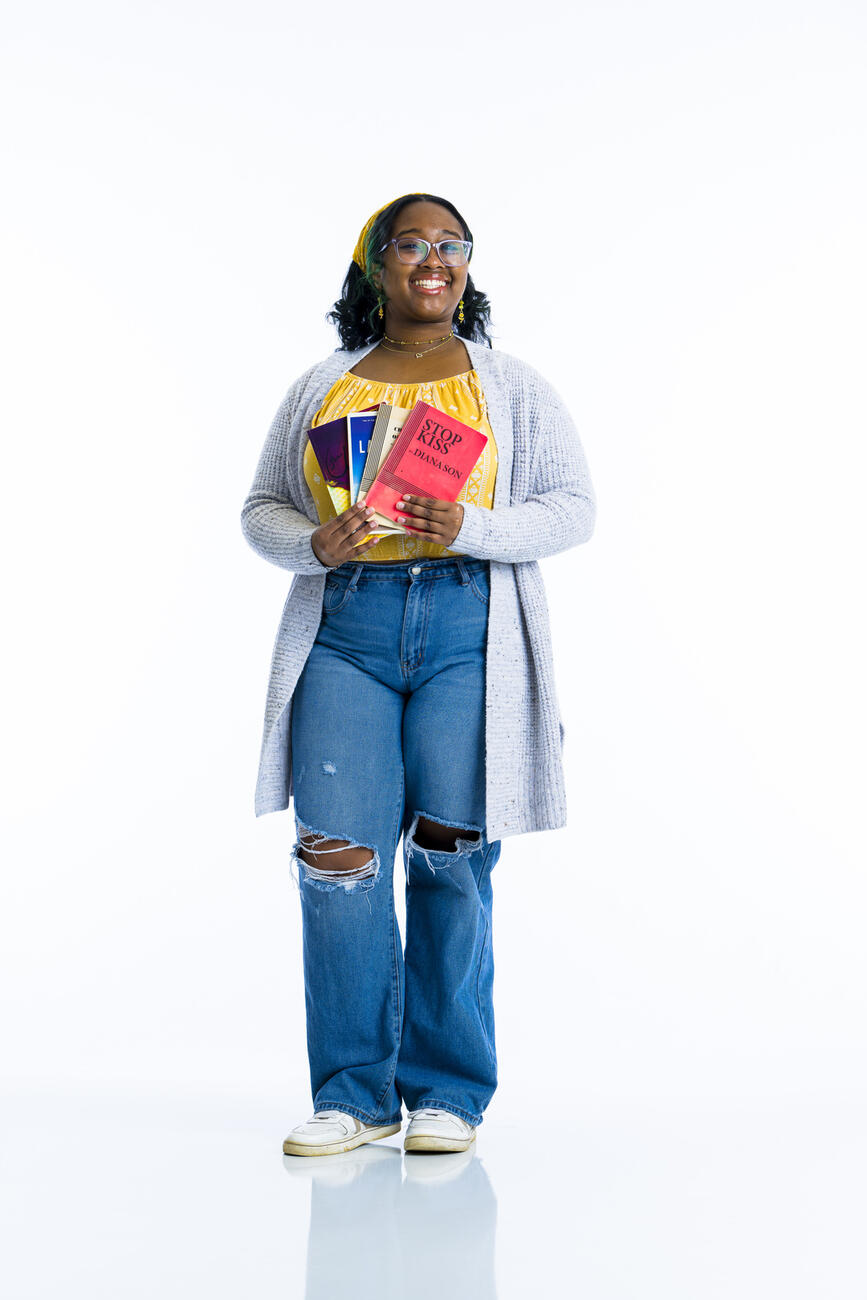 A student stands holding a set of playbills in front of her on a white background.