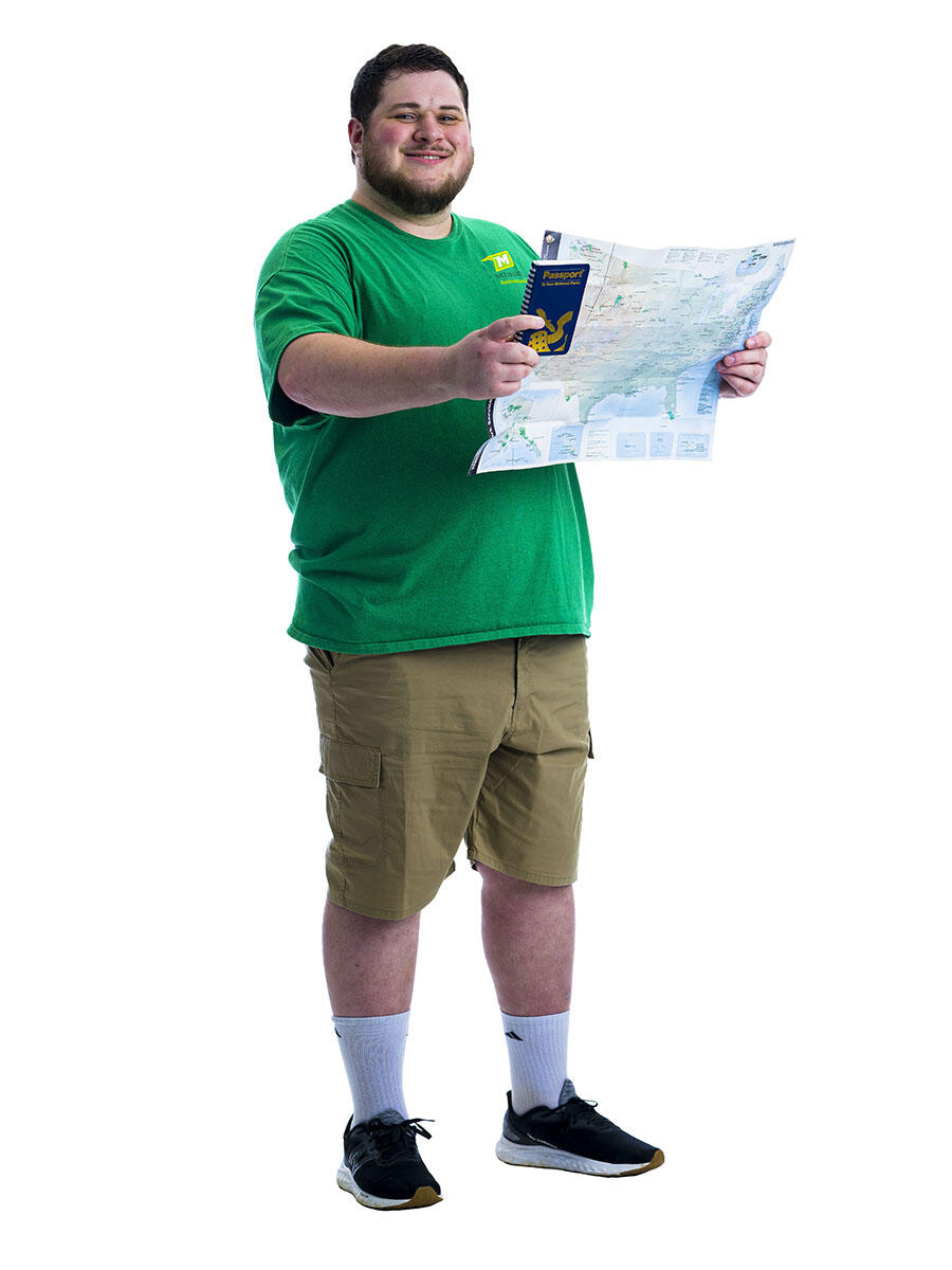 A student in a green shirt stands in front of white background while holding up a map.