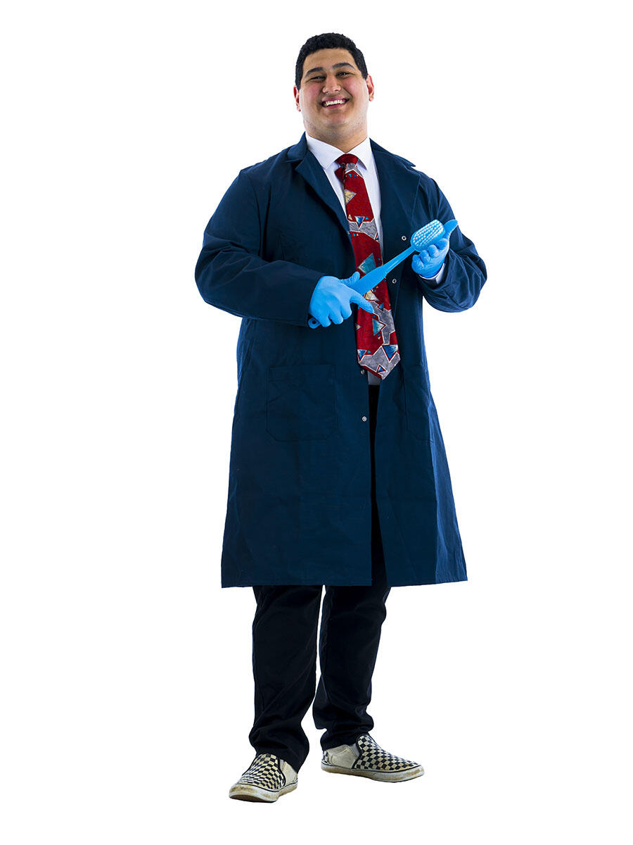 A student in dark blue lab coat poses with giant toothbrush against white background.