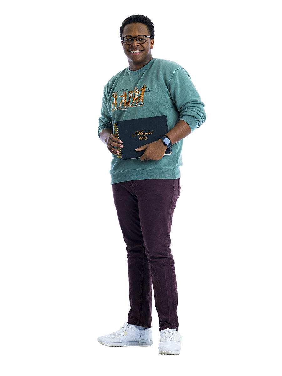 A student in a green sweatshirt holds a music book in front of a white background. 