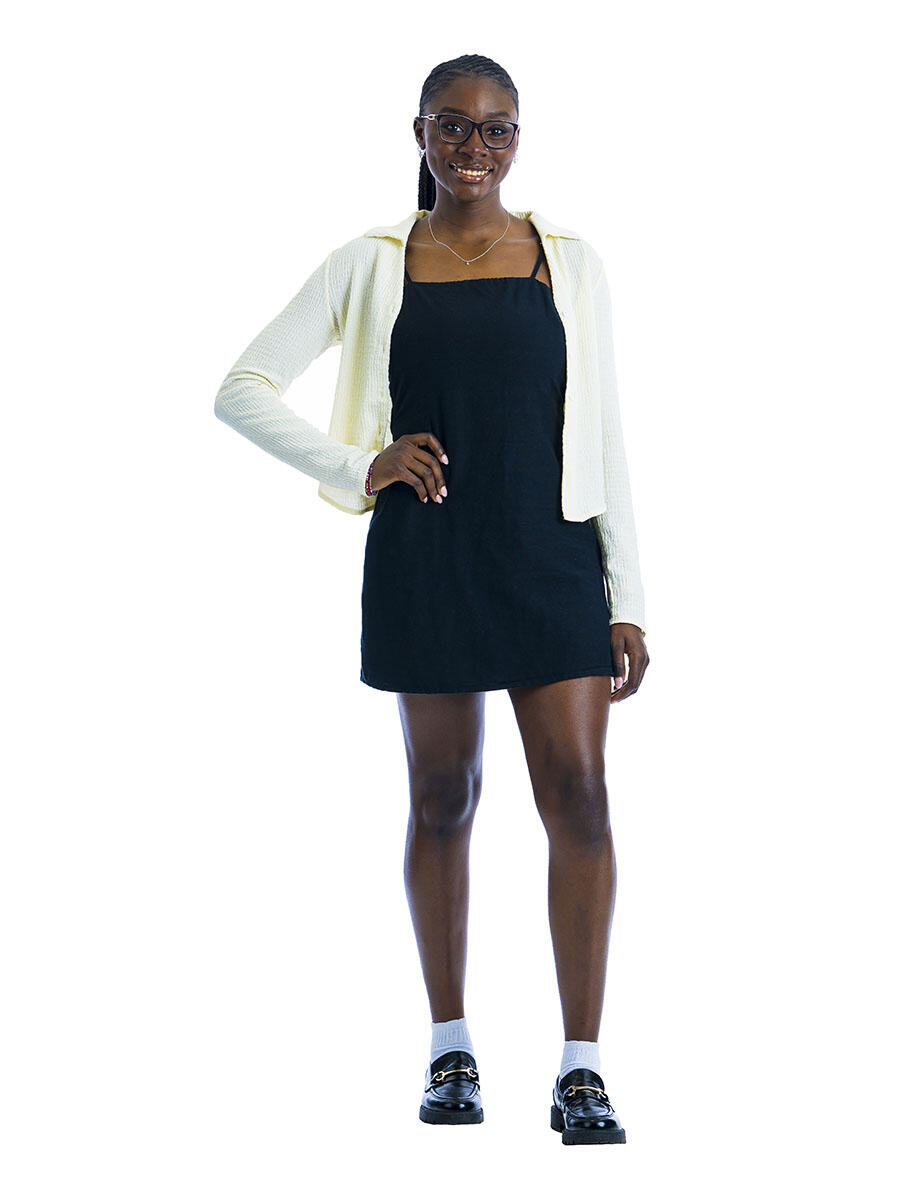 A student in a black dress and white cardigan stands with one hand on her hip in front of a white background.