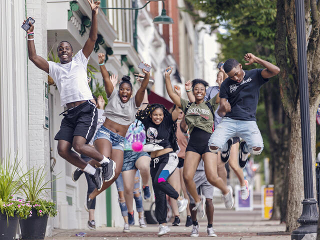 Students jumping in the air on a sidewalk in downtown Westminster. 