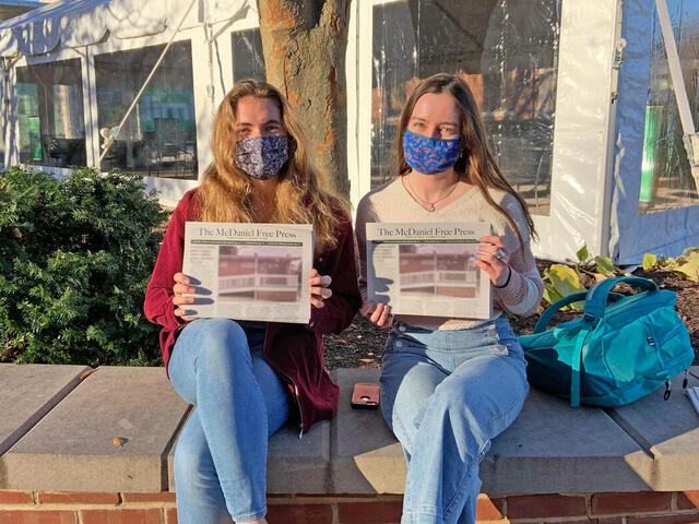 Two Free Press editors sit on a wall while holding up copies on the student newspaper.
