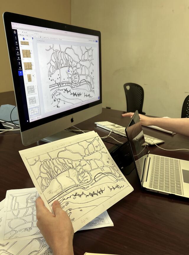 A hand holds a paper map while comparing it to a map on a computer screen.