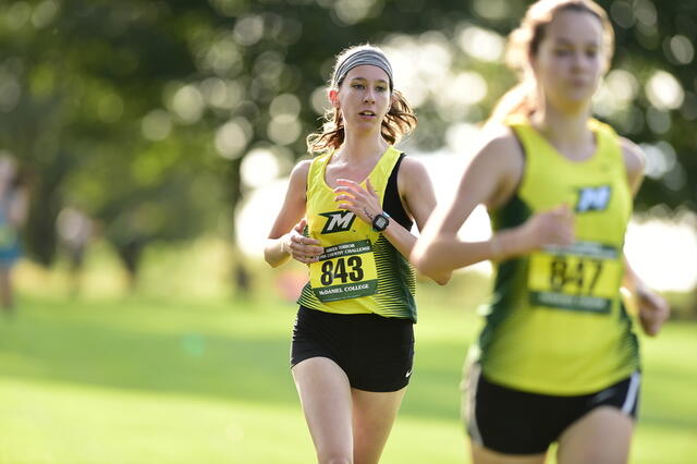 Photo of two female athletes running outside in McDaniel sports uniforms.