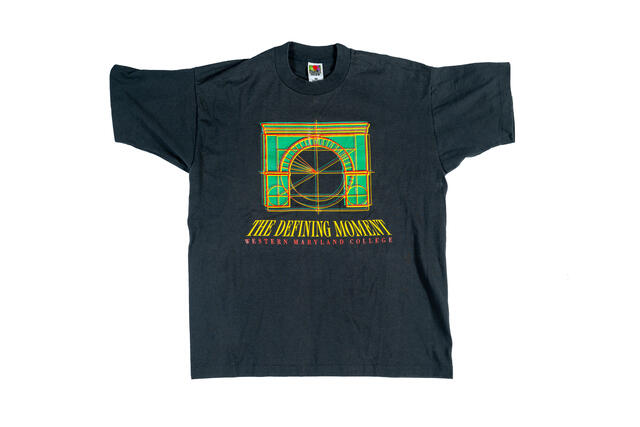Black t-shirt with a stylized green and yellow drawing of the memorial arch and text that reads The Defining Moment, Western Maryland College.