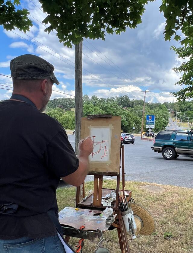 Professor Pearson paints an outline on an easel of a road and cars.