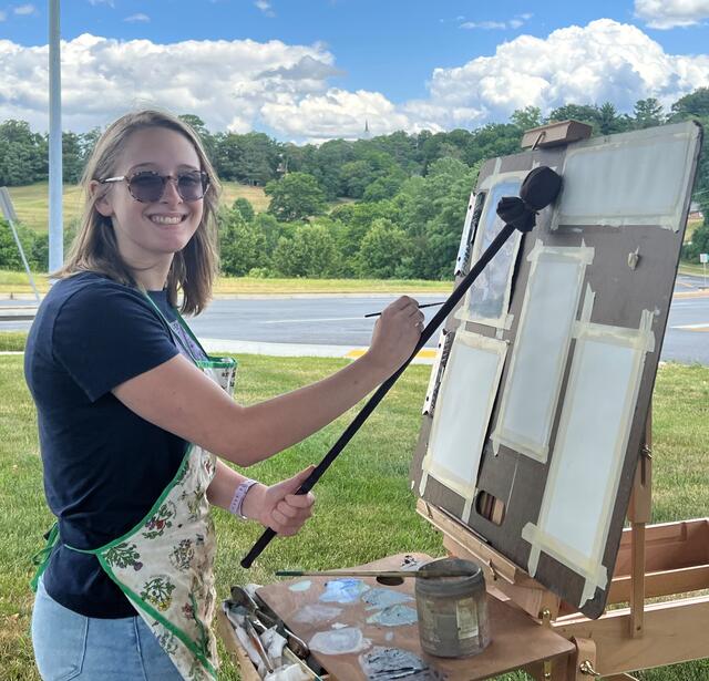 Zoe Shelby at her easel using a mahl stick to paint.