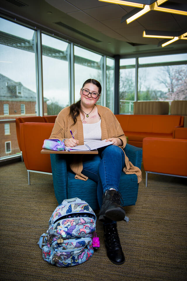 A student sits at a desk in the student center with a backpack at their feet.