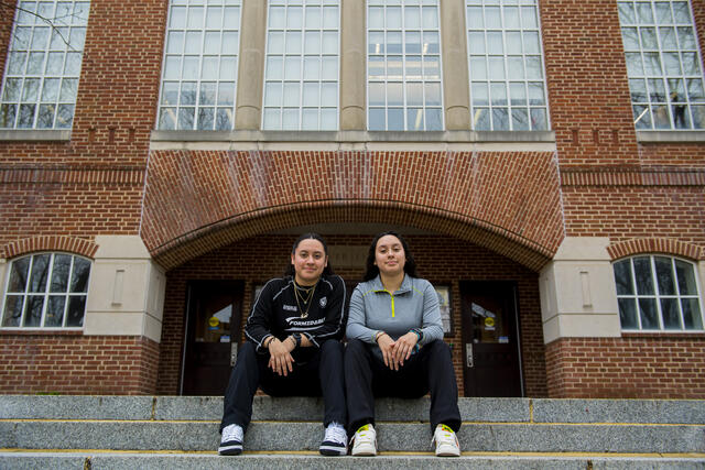 A pair of twins sits outdoors on the steps in front of McDaniel College's Hoover Library.
