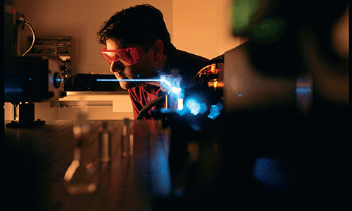 Professor Apollo Mian wearing shaded glasses while looking at laser instruments in McDaniel's optics lab.
