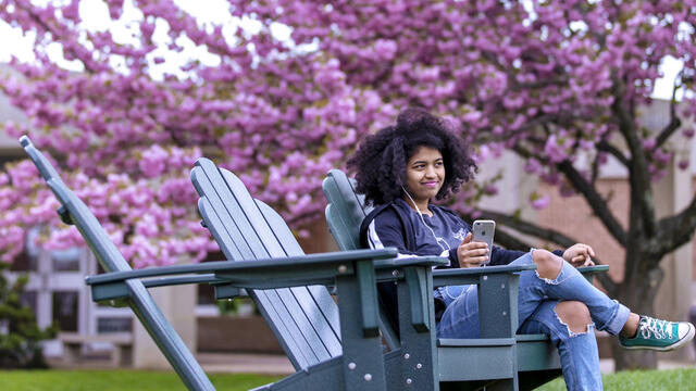 Student sitting in outdoor chair on campus listening to music.