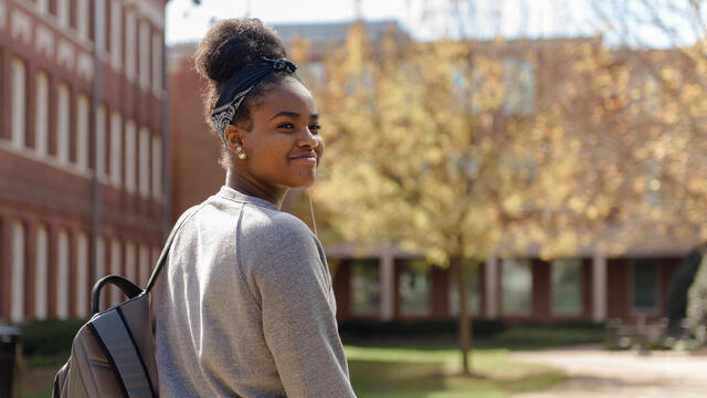 A student on campus looks back over her shoulder while smiling.