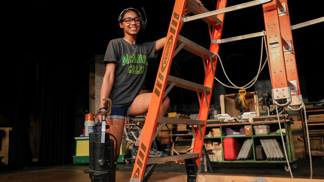Student Kim Parson climbs a ladder while holding a stage light.