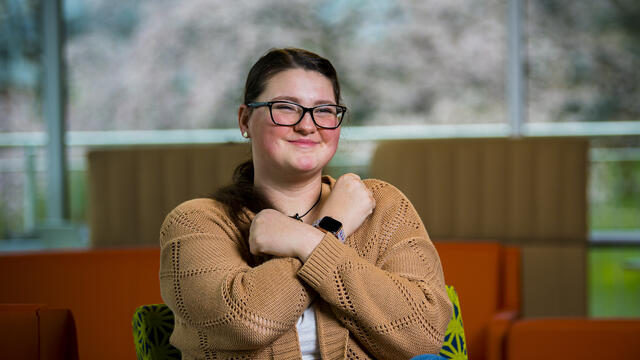 A student holds a pose in American Sign Language while sitting in the campus student center.