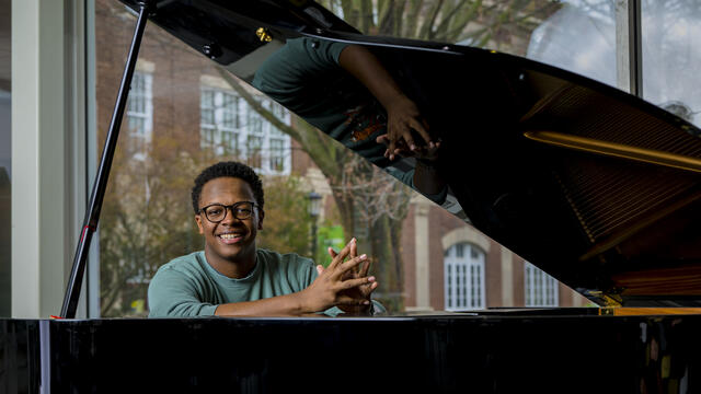 A student smiles while sitting at a piano.
