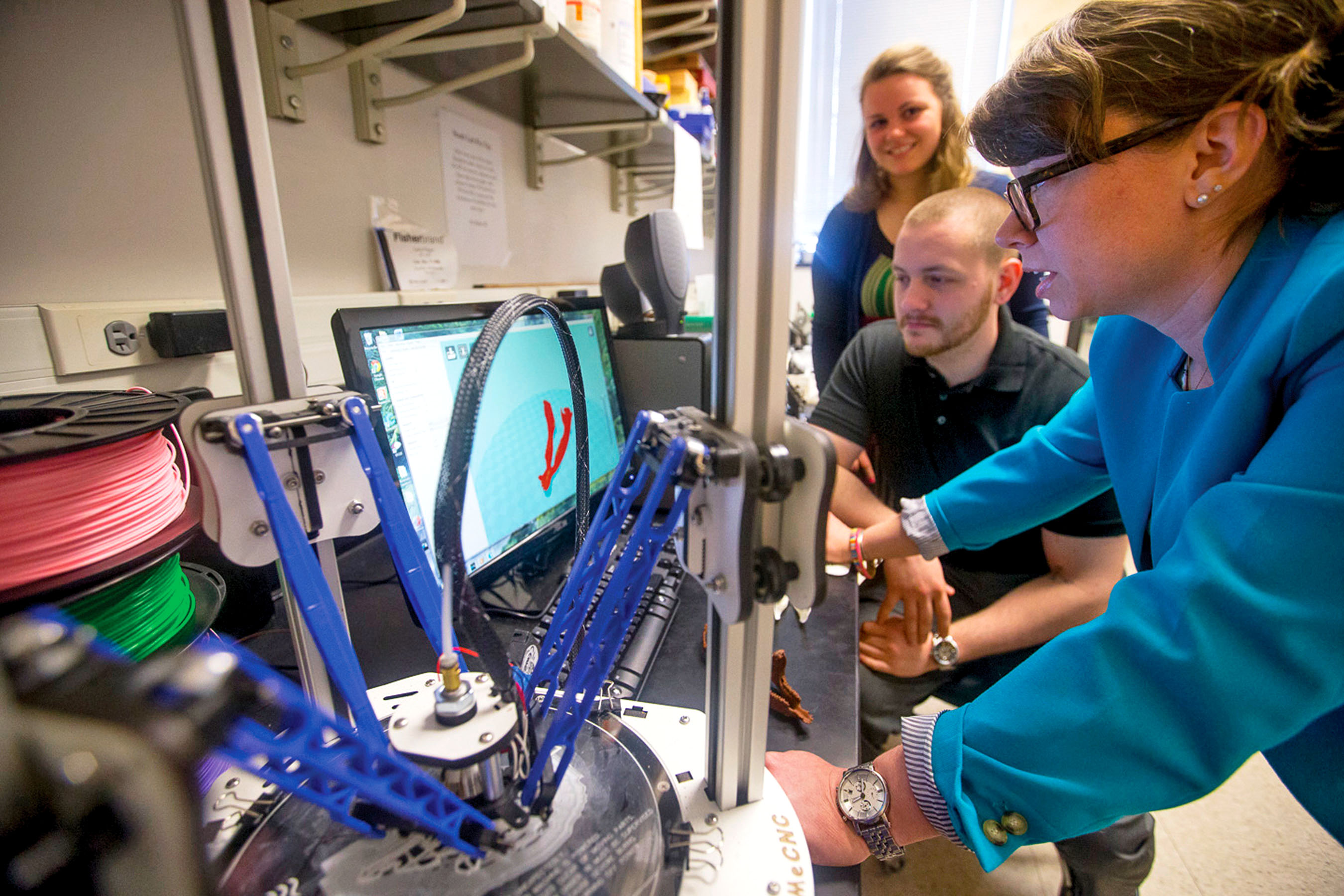 Biology professor guiding students in 3D printing.