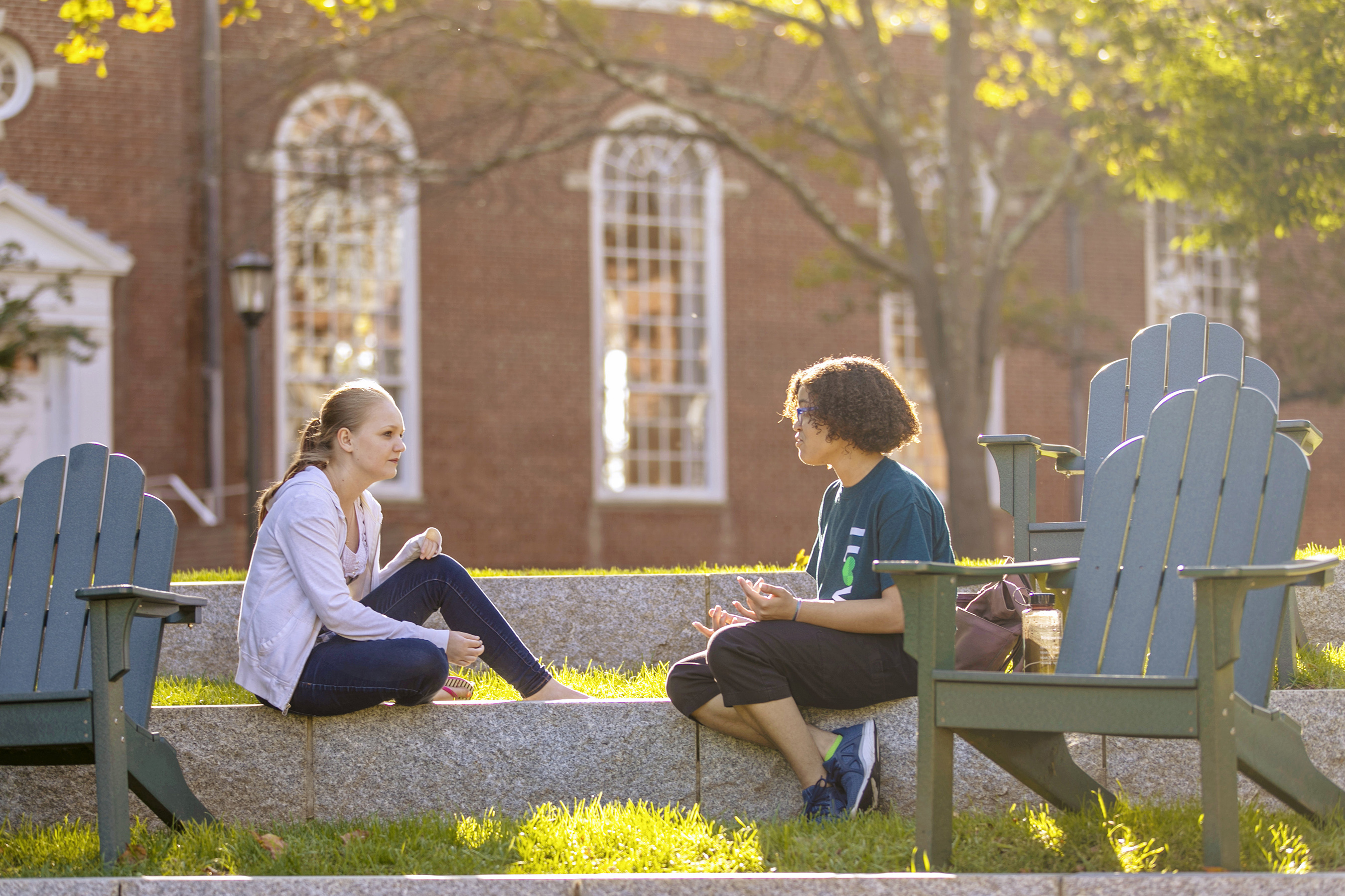 Students in conversation sitting near outdoor chairs.