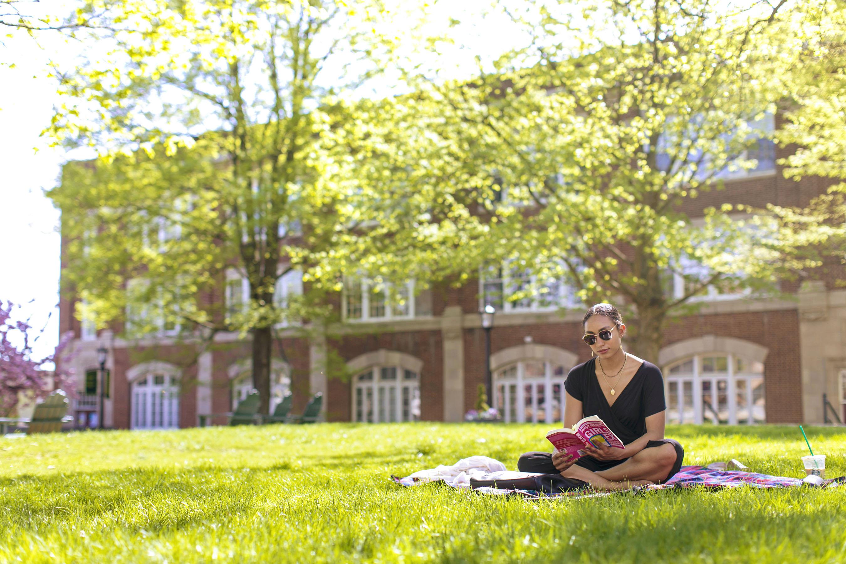 Student reading book sitting on lawn on campus.