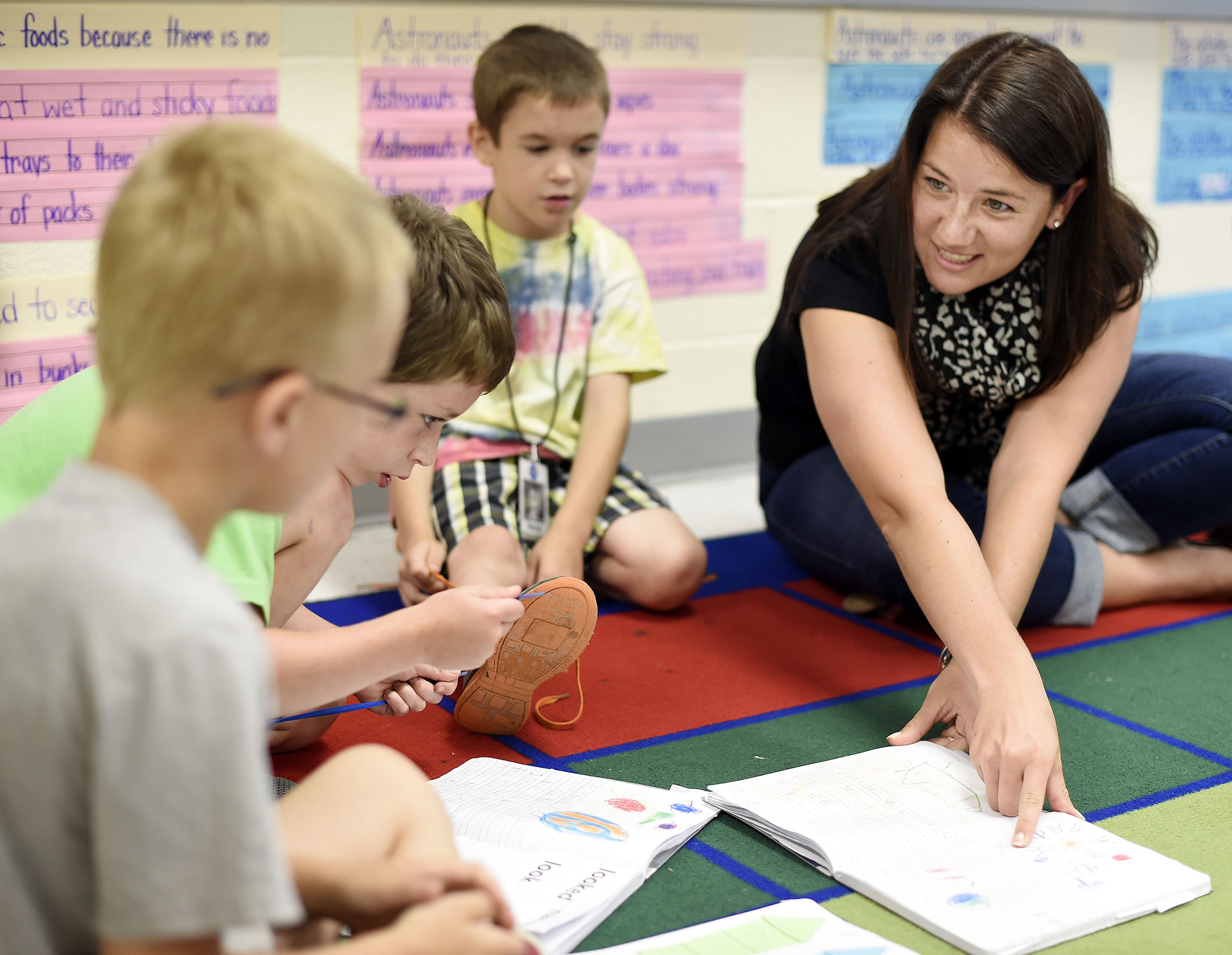 Student interacting with elementary school children on carpet.