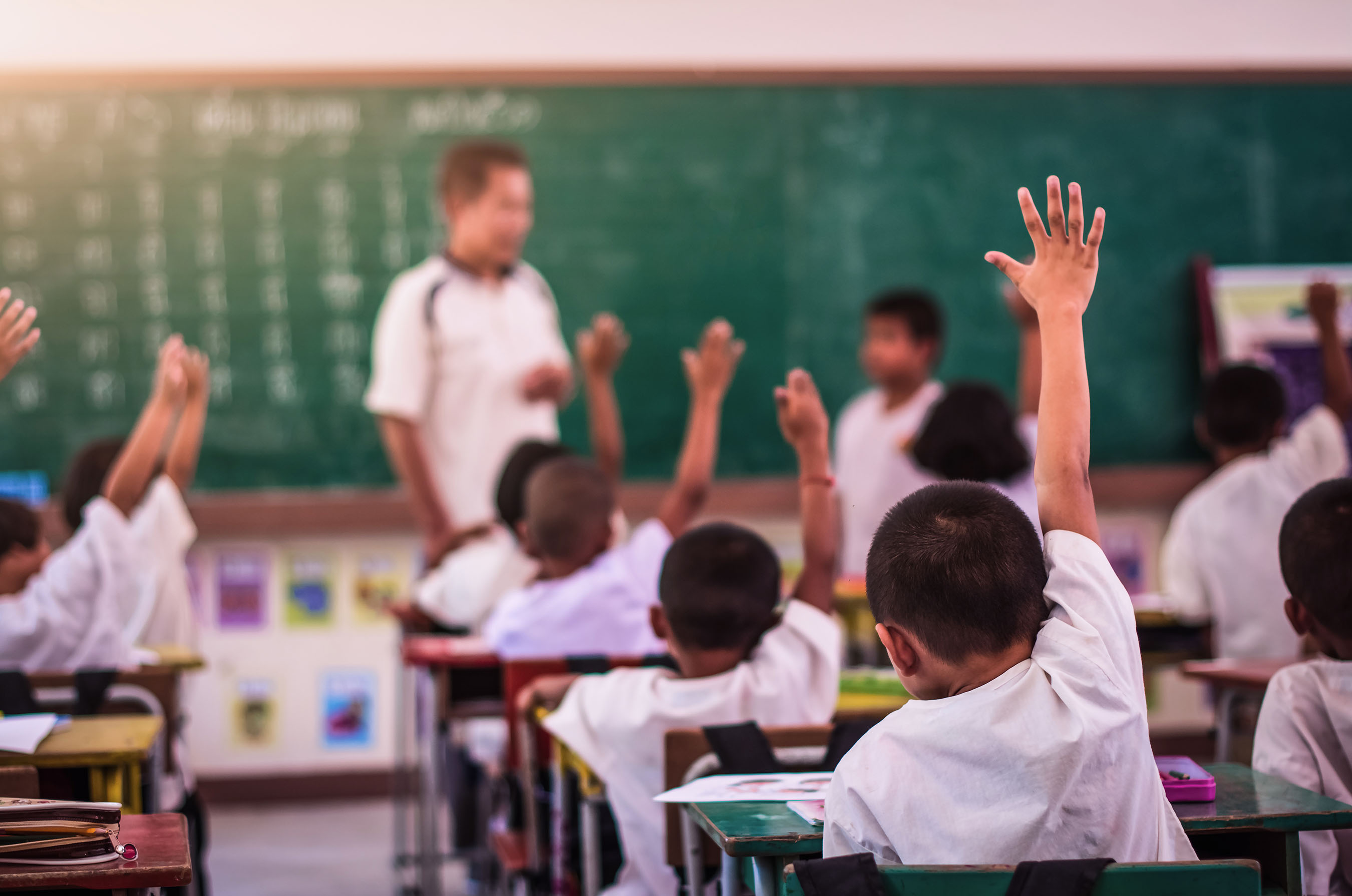 Elementary students raising their hands in classroom.