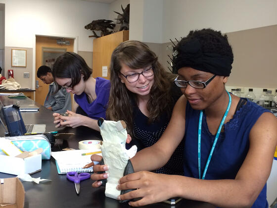 Favour Ubani (right) discusses her cell phone holder with professor Katie Staab while classmate Jillian Stewart works in the background.