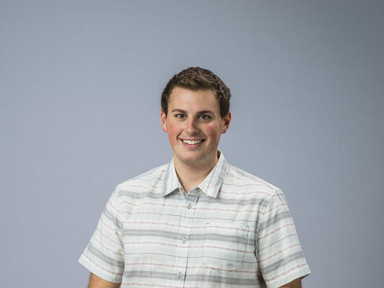 Newman Civic Fellow Atticus standing in front of plain background.