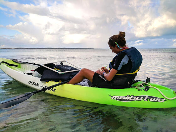 Jackie jotting notes in a kayak on the open water.