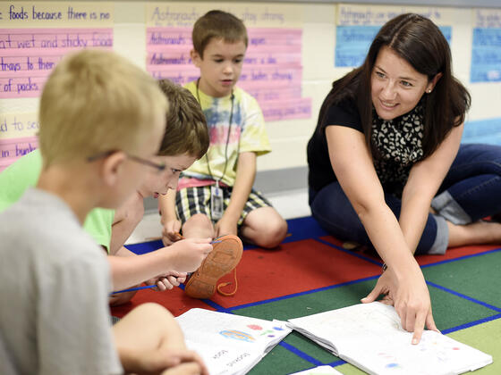 Student interacting with elementary school children on carpet.