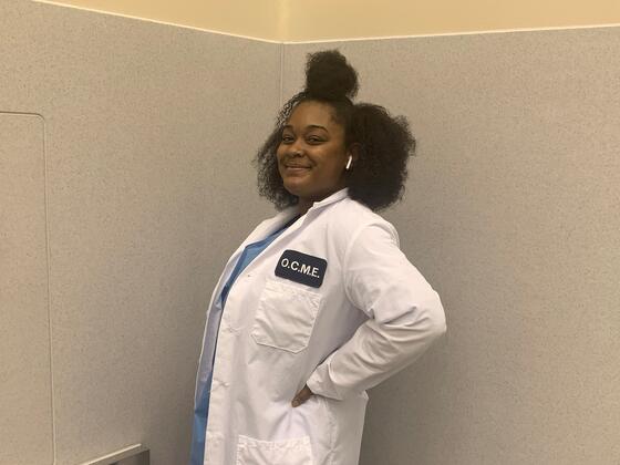 Alumni Treyana Johnson standing in her OCME lab coat.