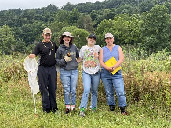 Three students pose with Holly Martinson in a field.