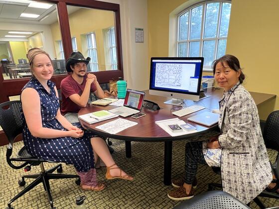 Two students sit with Professor Qin Fang in front of a computer that shows a map.