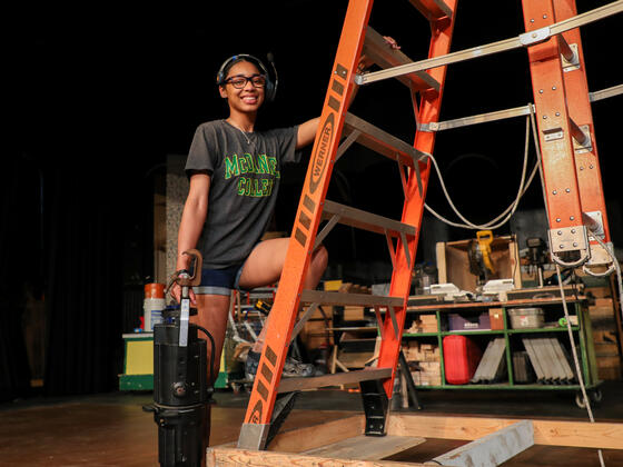 Student Kim Parson climbs a ladder while holding a stage light.