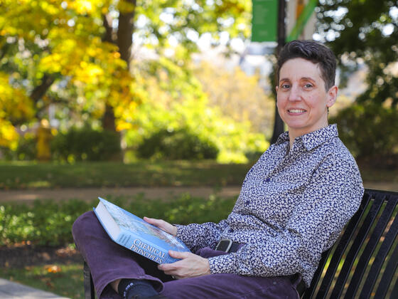 Chemistry professor Melanie Nilsson holding a Chemistry textbook while sitting on a bench outdoors.