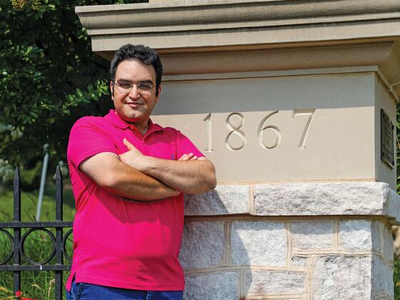 Photo of professor Farzad Ahmadi standing by a stone pillar on campus with 1867 inscribed on it.