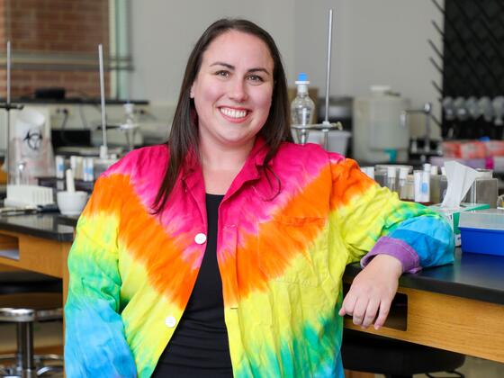 Photo of professor Maureen Williams in a tie-dyed lab coat sitting in a science lab.