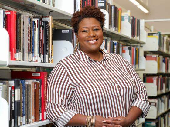 Photo of professor Shaeeda Mensah in front of a bookcase in the library.