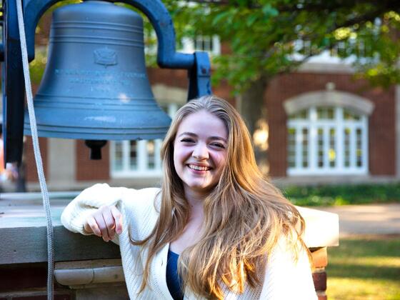 A blonde woman standing by a bell outside 