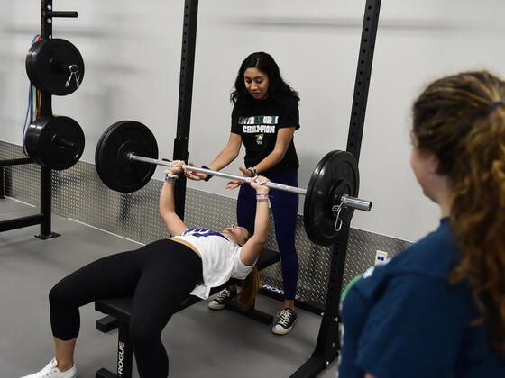 Photo of a woman helping another woman use a bench press.