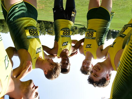 Photo of a group of students huddled at a cross country track meet.