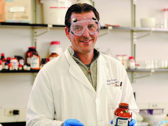 Photo of professor Dana Ferraris in a lab coat and gloves holding a bottle in a lab.